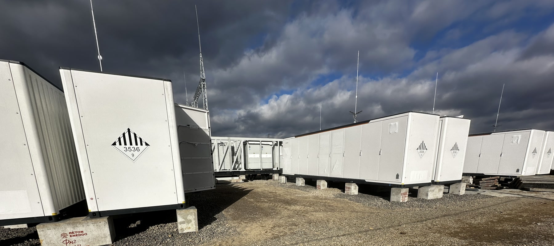 Rząd białych kontenerów magazynu energii BESS na placu budowy pod zachmurzonym niebem