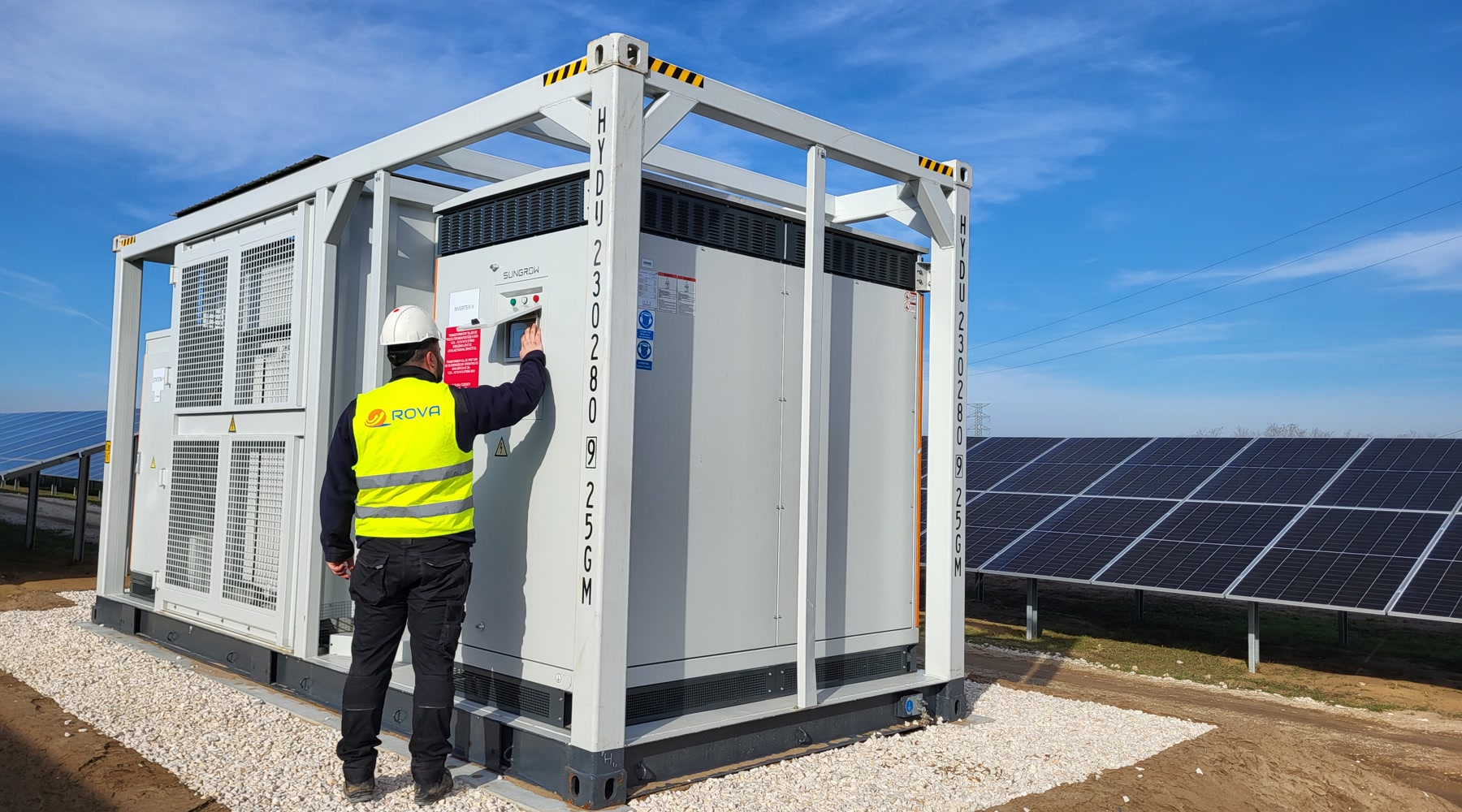 Technik ROVA obsługujący panel sterowania kontenera PV i BESS na farmie fotowoltaicznej